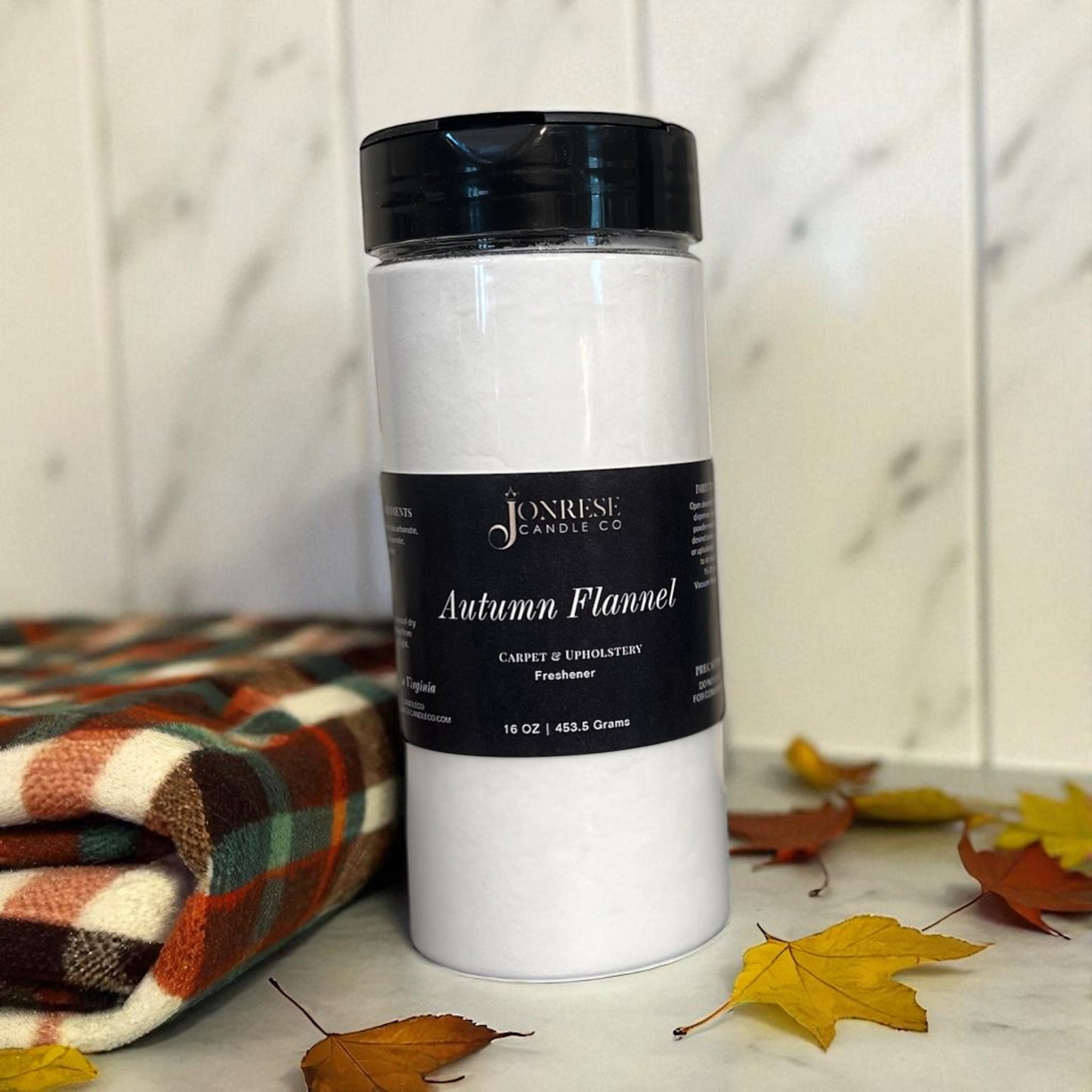 White container with black lid labeled 'Autumn Flannel' on a marble surface with leaves and a plaid blanket.