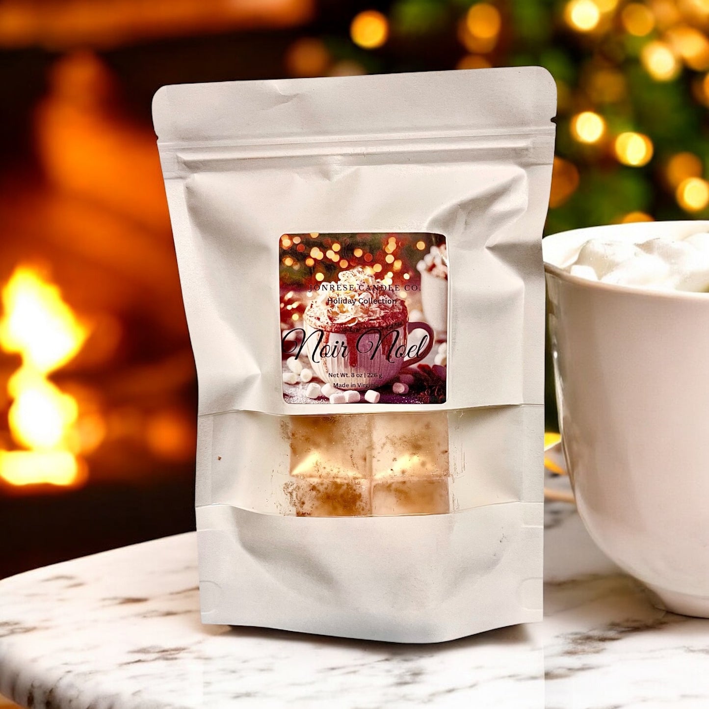White packaging of 'Noir Noel' with a Christmas-themed label, placed on a surface with a blurred background of lights and fire.