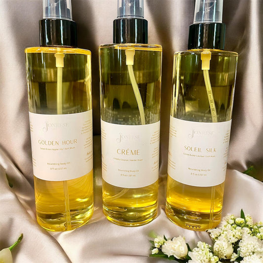 Three bottles of body oils with floral decorations on a light fabric background.