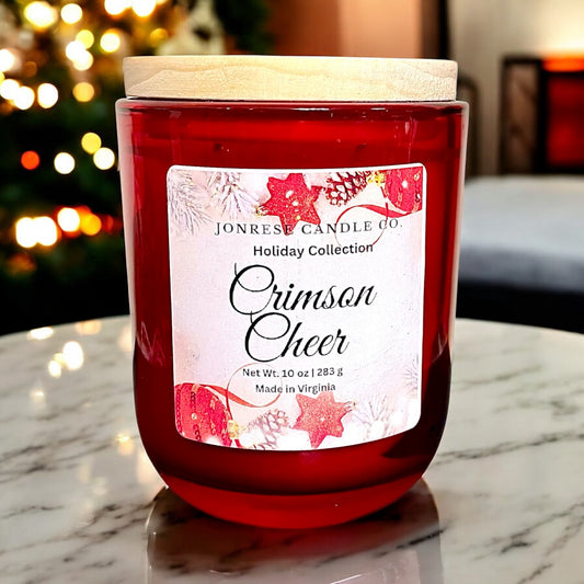 Red candle labeled 'Crimson Cheer' from Jonrese Candle Co on a marble surface with blurred festive background