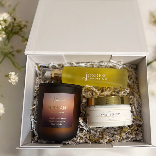 Jonrese Candle Co products including a candle, jar of body lotion and a bottle of body oil in a white gift box with flowers around it.