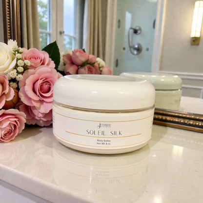 White jar of 'Soleil Silk' body butter on a bathroom counter with flowers in the background