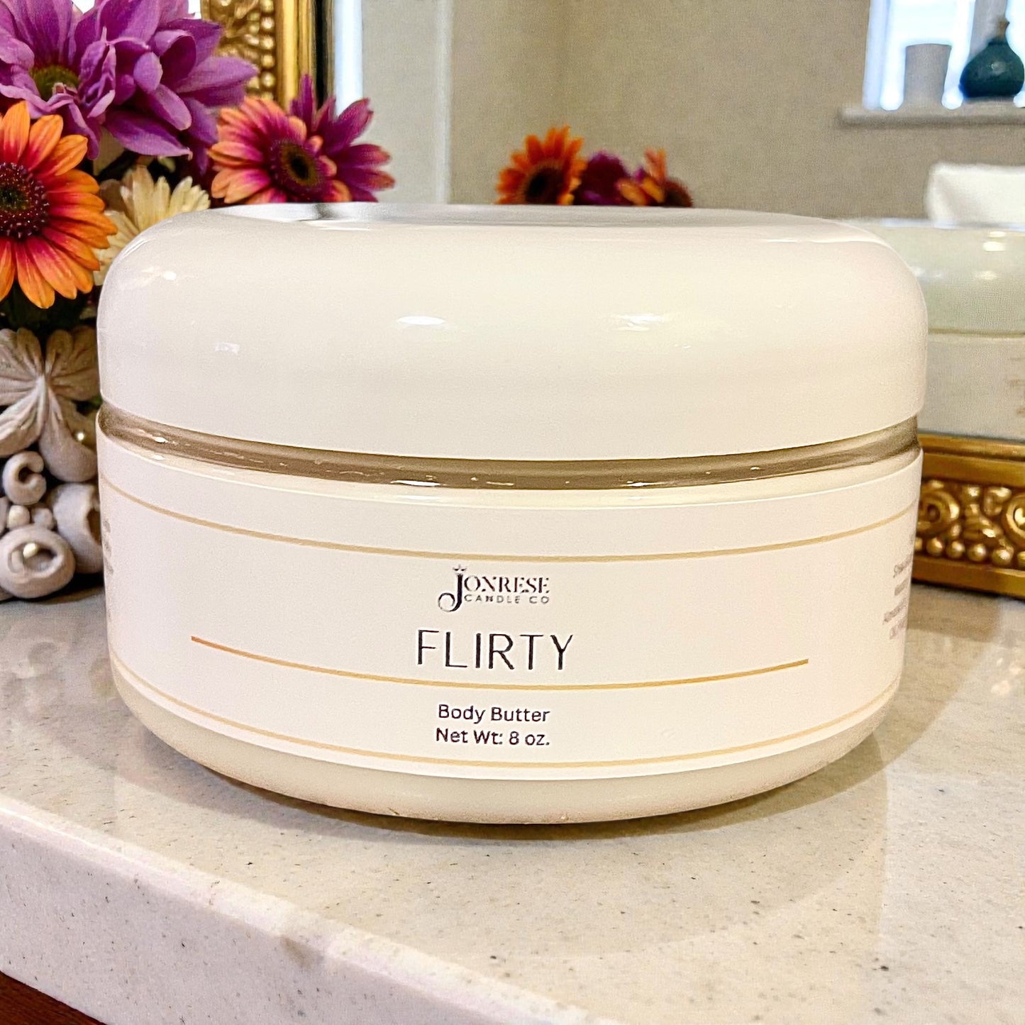 White jar of Jonrese 'Flirty' body butter on a counter with flowers in the background