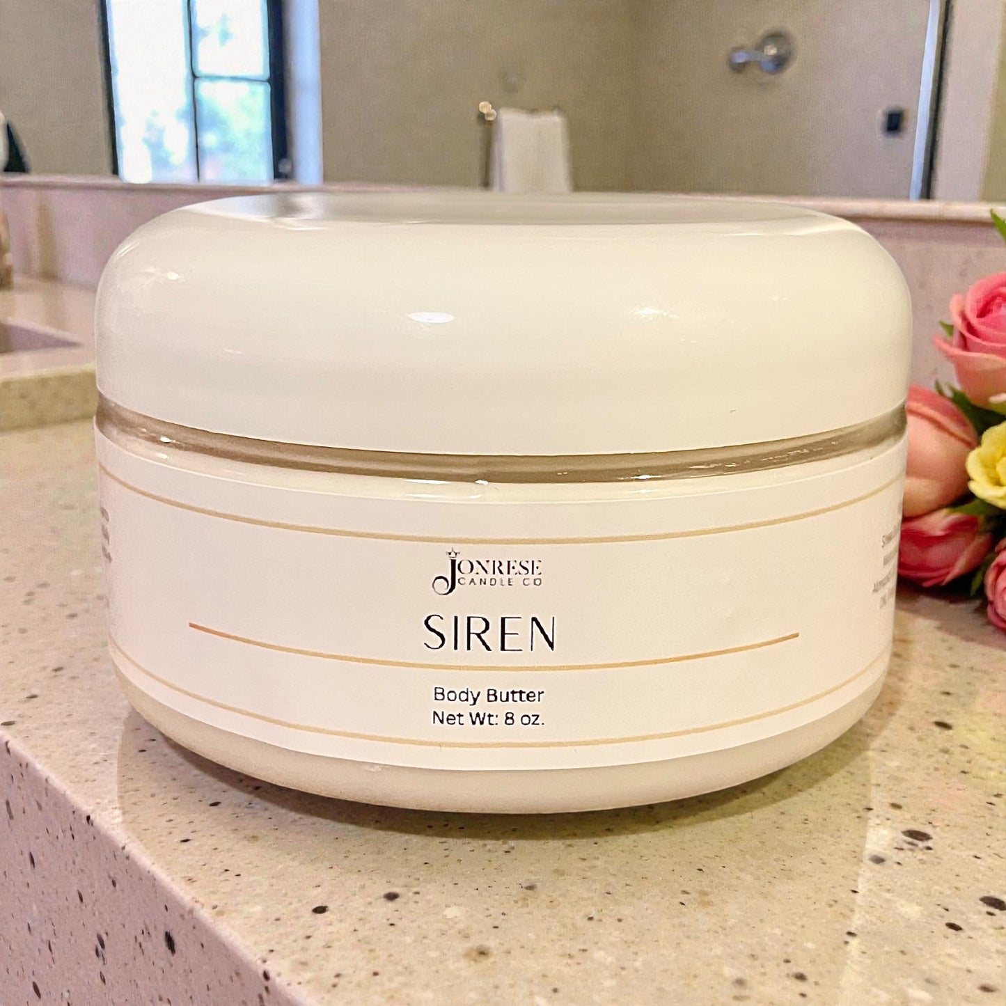 White jar of Siren body butter on a bathroom counter with flowers in the background