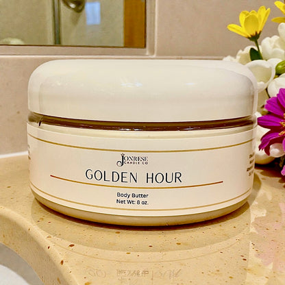 White jar of 'Golden Hour' body butter on a bathroom counter with flowers in the background
