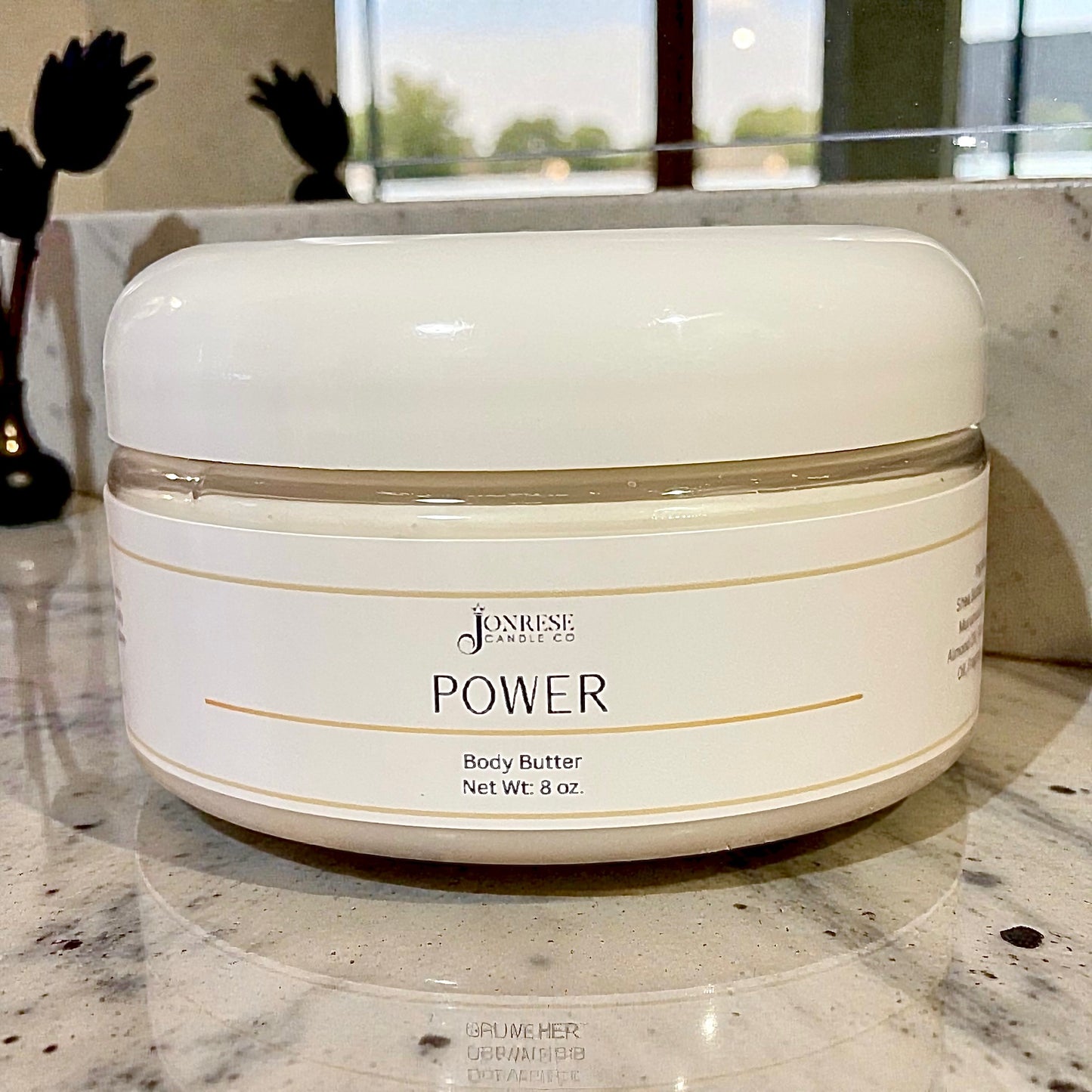 White jar of Jonrese 'Power' body butter on a marble surface with decorative elements in the background.