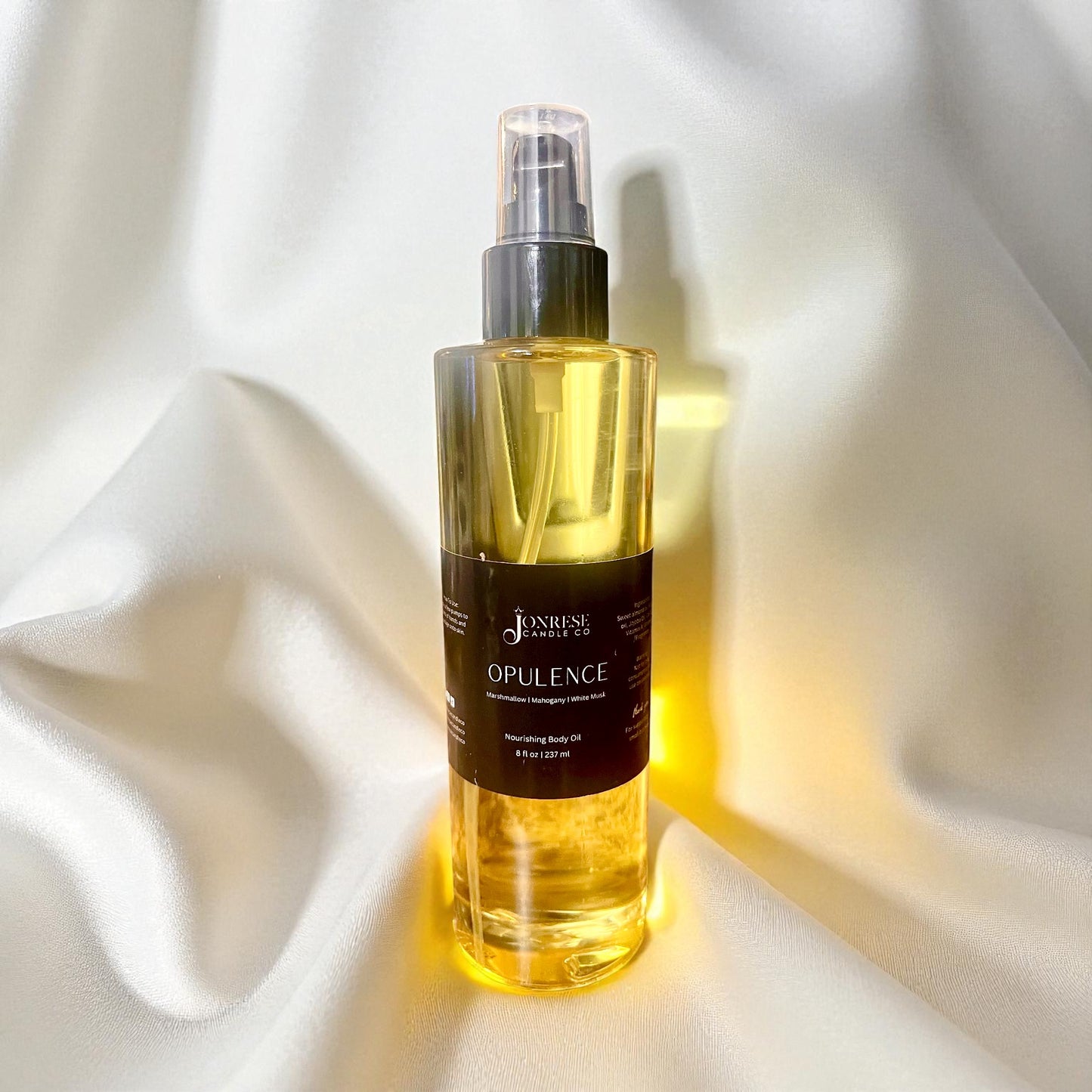 Bottle of 'Opulence' body oil on white silk fabric