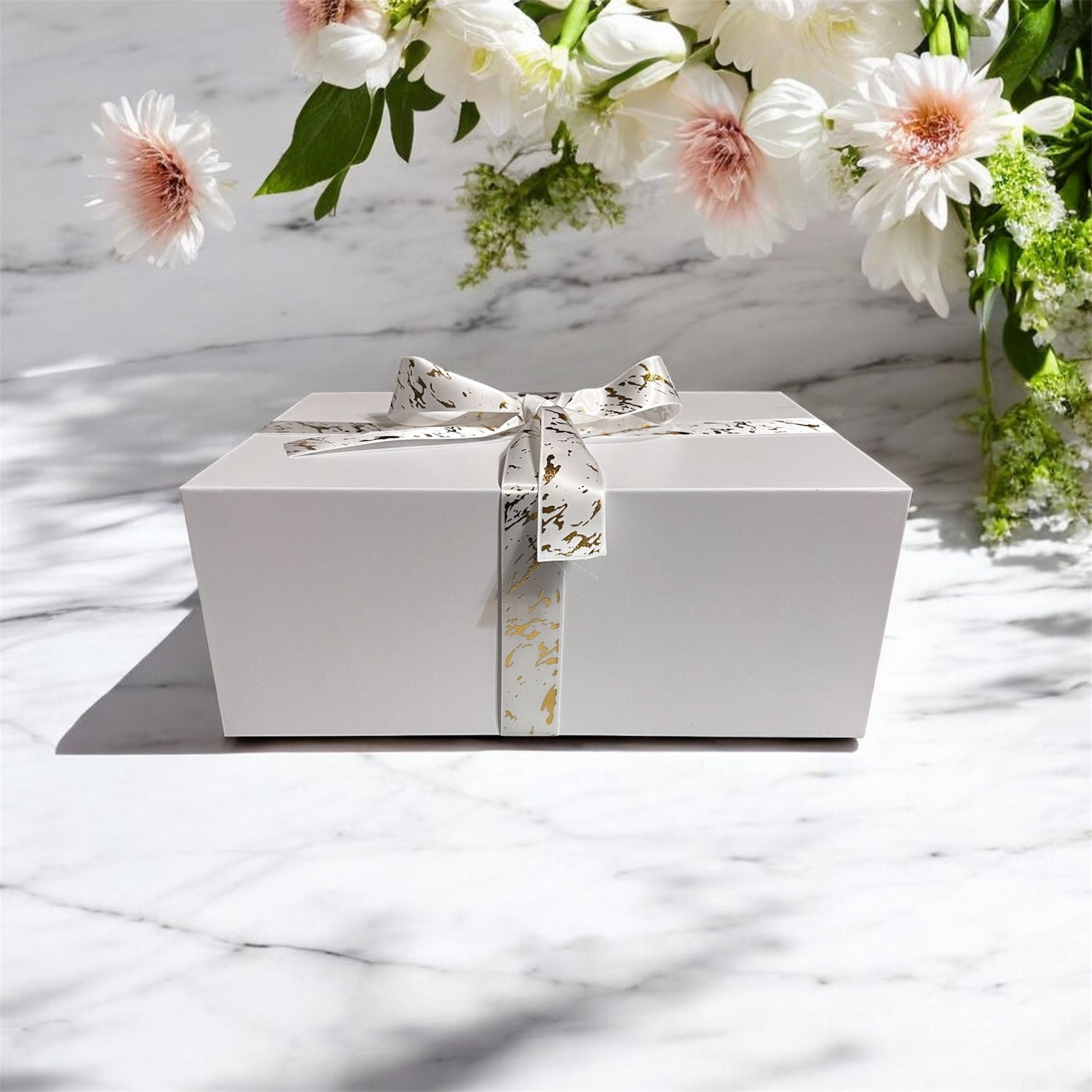 White gift box with a floral ribbon on a marble surface with flowers in the background