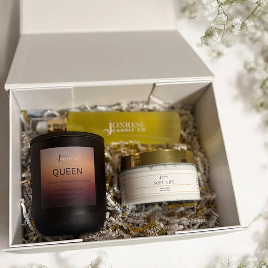 Jonrese Candle Co products including a candle, jar of body lotion and a bottle of body oil in a white gift box with flowers around it.
