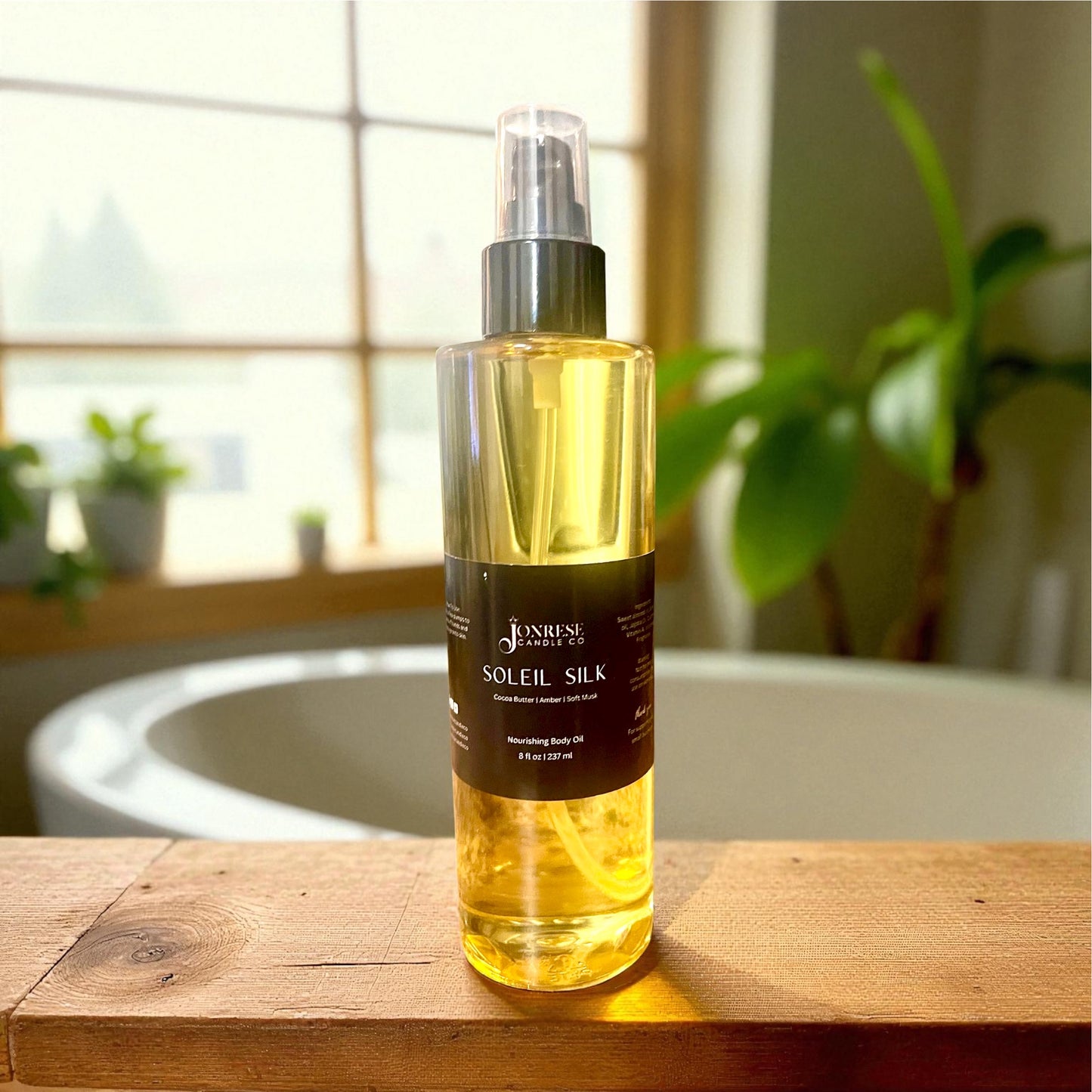 Bottle of 'Soleil Silk' body oil on a wooden surface with a blurred background of a bath tub, window and plants 